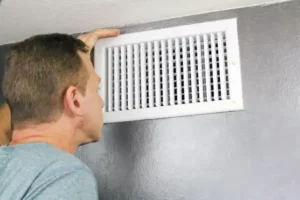 A man inspecting a wall-mounted air vent.