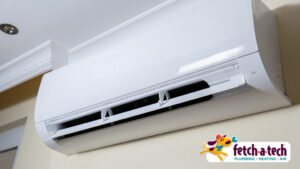 A wall-mounted air conditioning unit with a white exterior, placed beneath a ceiling. A "fetch-a-tech" logo is visible in the bottom right corner.