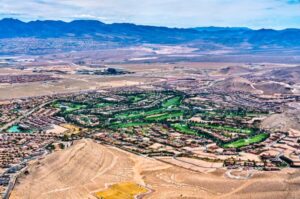 Aerial view of a desert landscape with a residential area and a lush green golf course, featuring glimpses of top-notch plumbing and HVAC systems in Southern Highlands, all surrounded by arid hills and distant mountains under a clear sky.