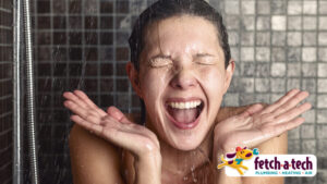 Person smiling with eyes closed under a shower. Water droplets are visible. Bottom right shows a Fetch-A-Tech logo with a dog and the text "Plumbing - Heating - Air.