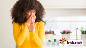 Person in a yellow sweater covering nose, with potted plants on a shelf behind. Fetch-a-Tech logo is in the corner.