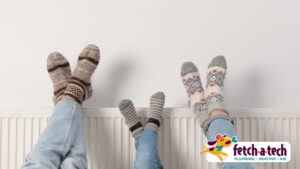 Three people wearing patterned socks rest their feet on a radiator. A logo in the bottom right corner reads "fetch-a-tech Plumbing, Heating, Air.